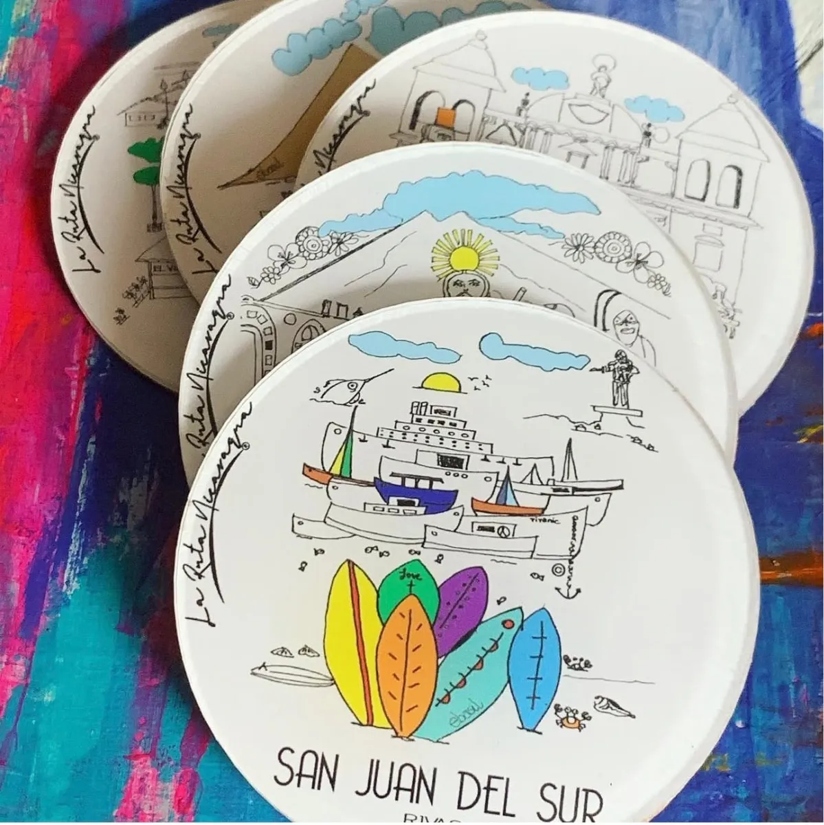A stack of ceramic plates illustrated by Elsa Basil, the top one lettered San Juan del Sur above a row of surfboards