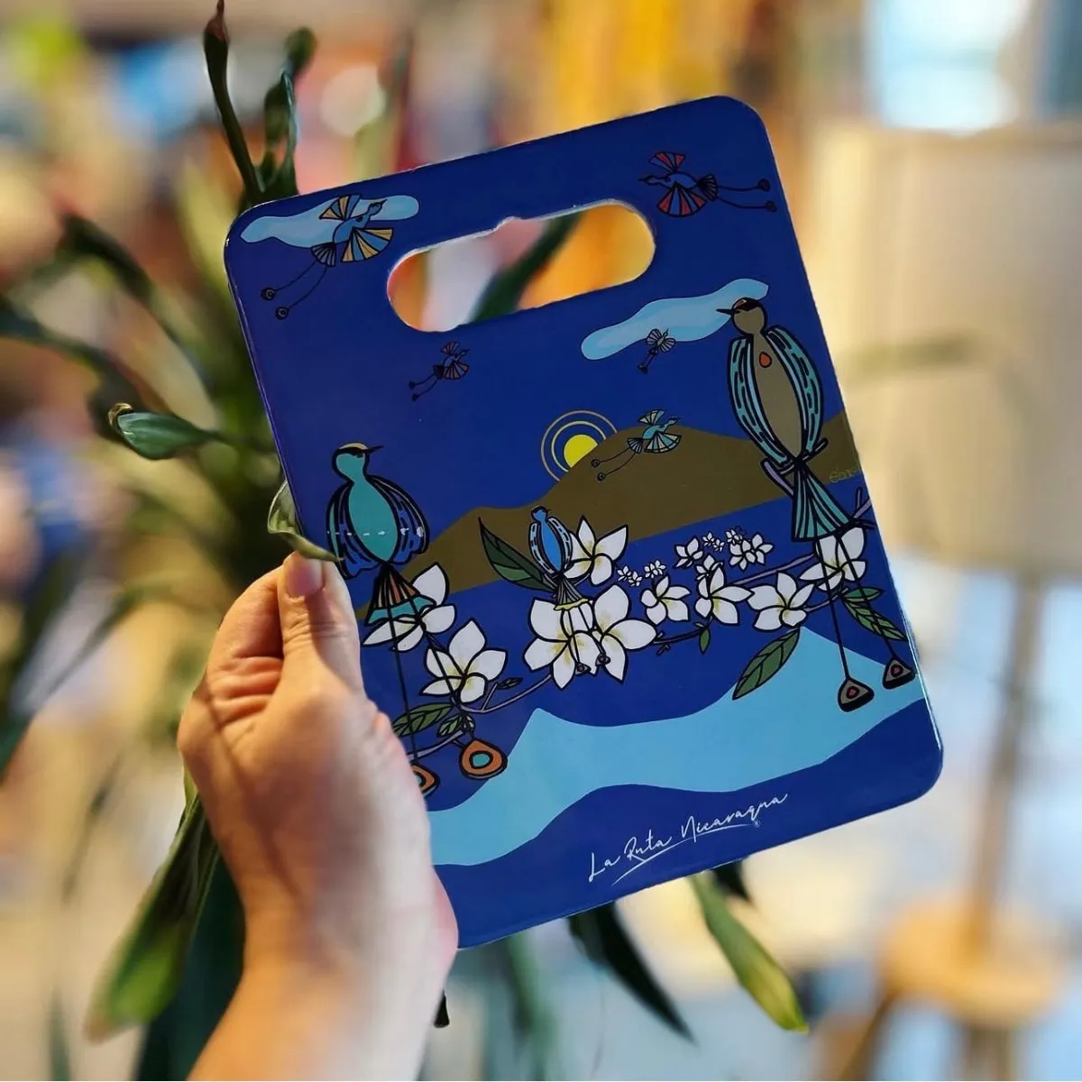 A hand holding a deep blue serving board illustrated with birds and white flowers